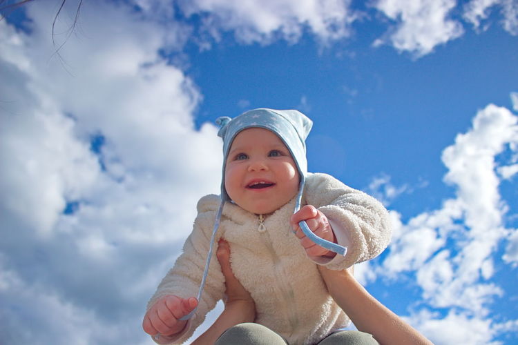 Cropped hands of parent holding cheerful toddler daughter against blue sky