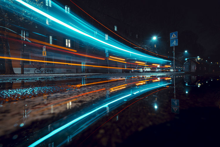 Light trails at night reflecting in a puddle after rainfall