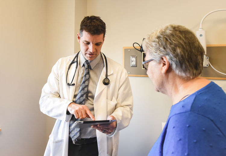 Doctor holding tablet speaking to older patient in a clinical setting.