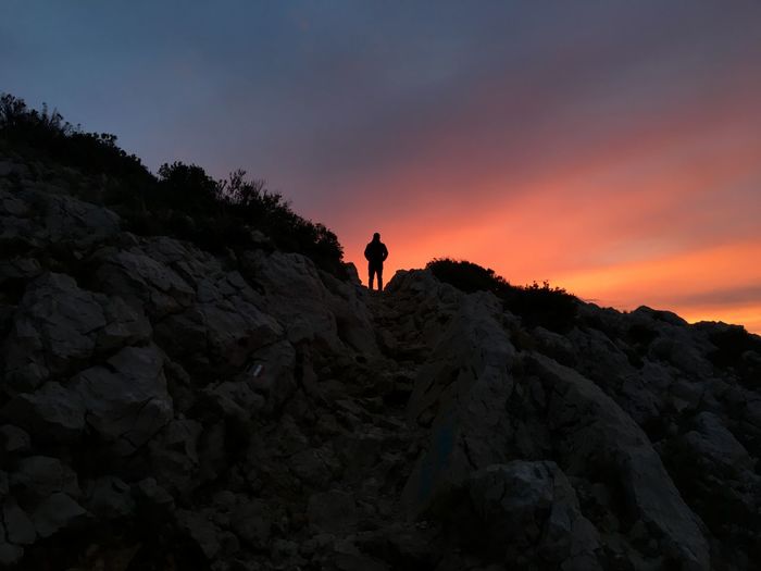 Silhouette person on rock against sky during sunset