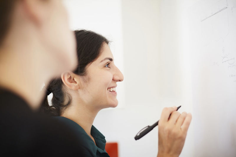 Smiling mid adult woman holding pen while looking at whiteboard in office