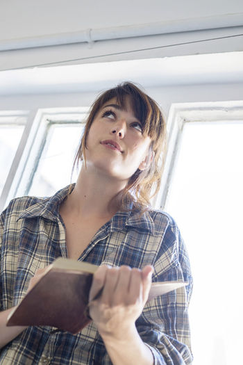 Young woman holding diary while looking up at home