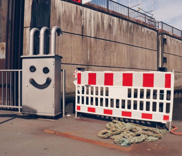 Anthropomorphic smiley face on metallic container by barricade on street