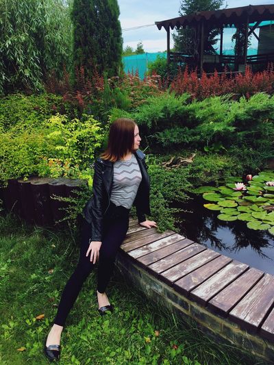 Full length of young woman sitting by pond