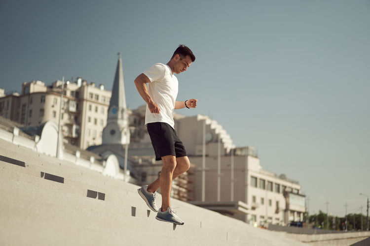 Side view of athletic male running downstairs while training on sunny day in city in summer
