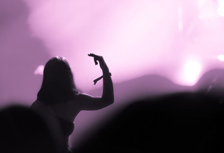 Silhouette woman with arms raised standing at music concert