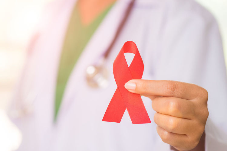 Midsection of doctor holding red ribbon