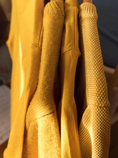 Yellow illuminated color winter sweaters on wooden hangers. trendy fashion autumn cozy clothes.