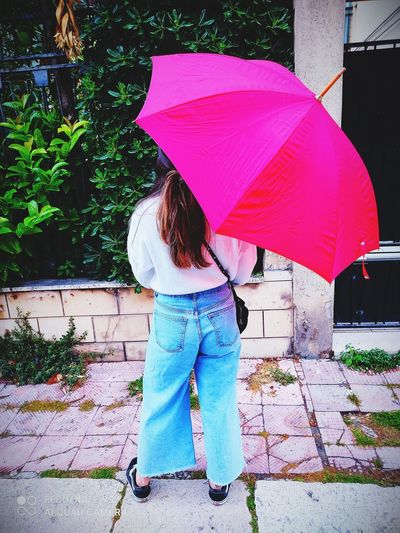 Person holding umbrella standing on footpath during rainy season