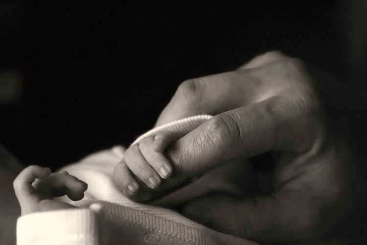 Cropped image of person holding baby hands against black background