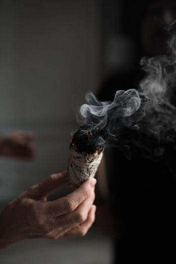 Woman hand holding herb bundle of dried sage smudge stick smoking