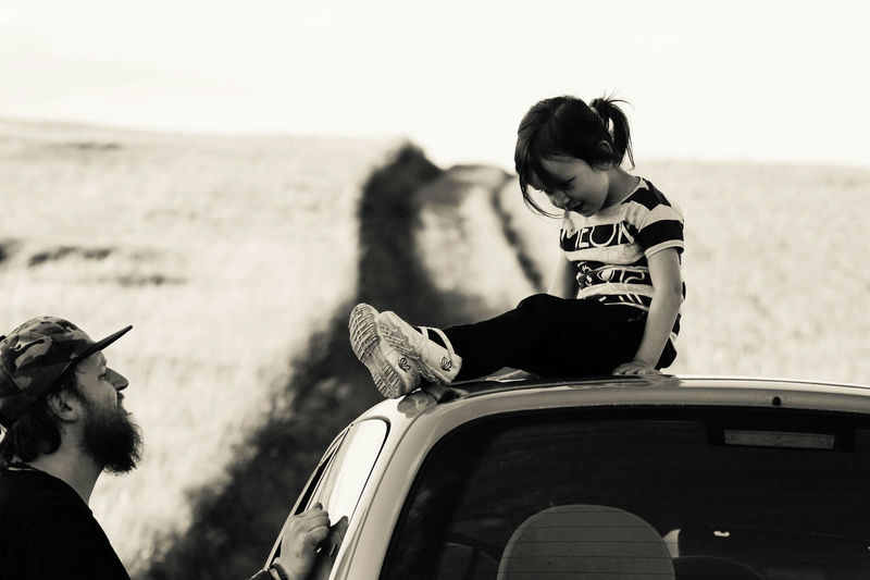 Side view of man looking at daughter sitting on car roof