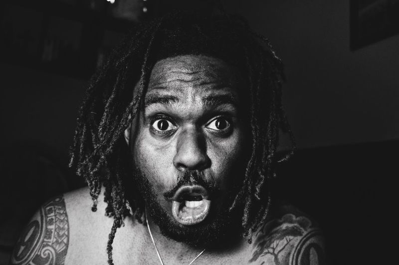 Close-up portrait of shocked man with dreadlocks at home