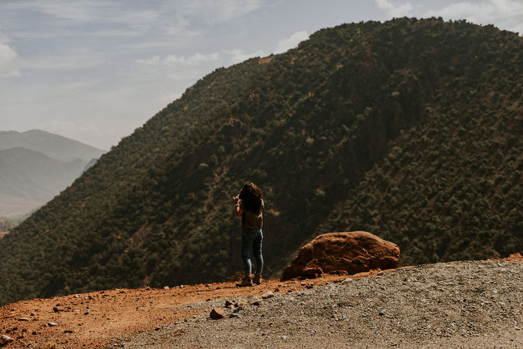 Rear view of woman standing on rock against mountain