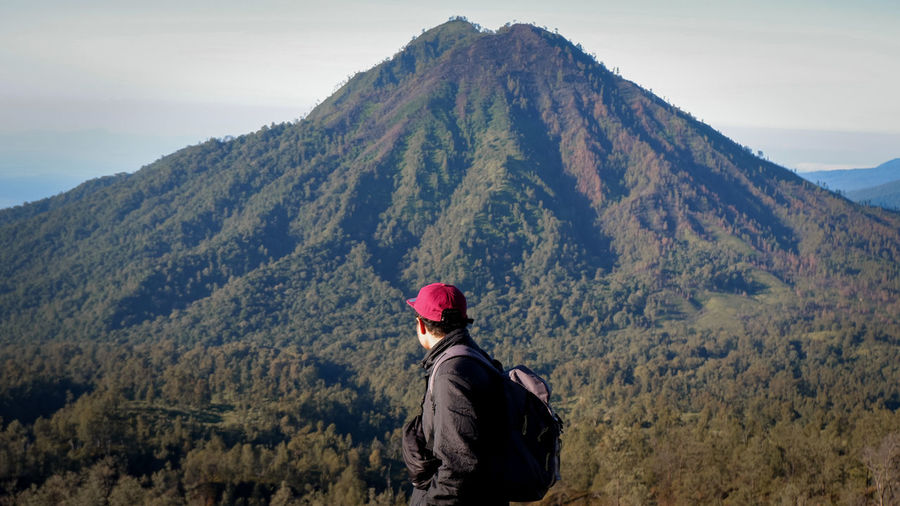 Side view of young man looking at mountain against sky