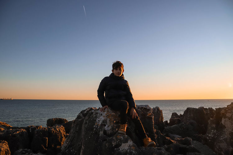 Man sitting on rock by sea against clear sky