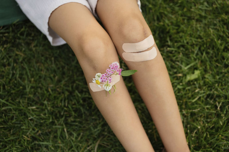 Girl with knees taped by bandage and flowers sitting on grass