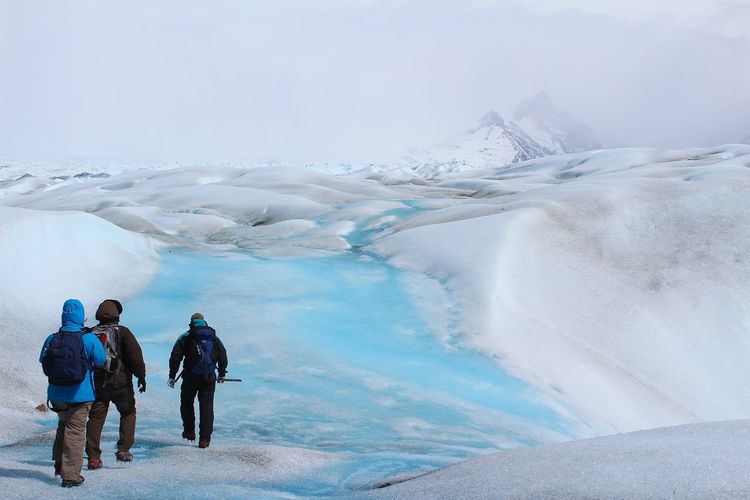 Rear view of people walking on glacier