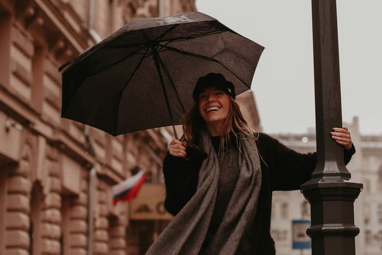 Portrait of a young woman in a cozy black autumn coat and a gray scarf walking with an umbrella 
