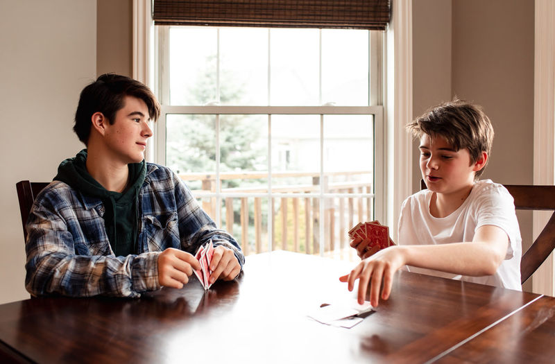 Two teenage boys playing cards at the kitchen table together.