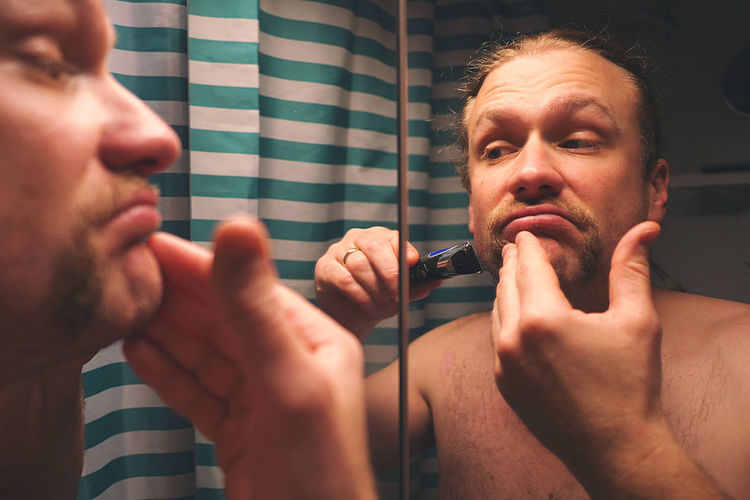 Reflection of man in mirror shaving in bathroom