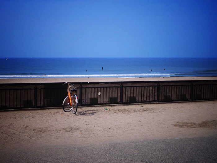 Man cycling on beach against clear blue sky