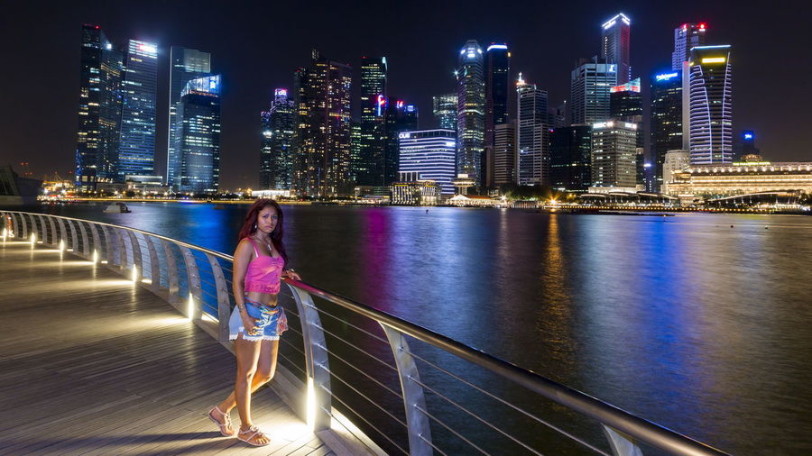 Woman standing on promenade by river in city at night