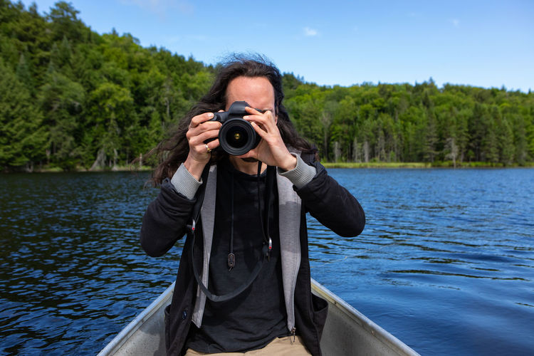 Portrait of man photographing against lake