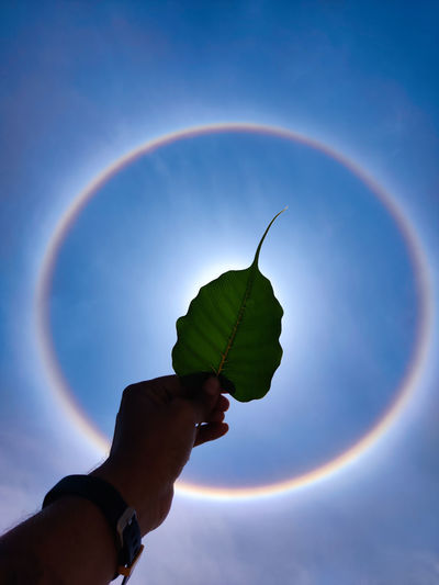 Midsection of person holding rainbow against blue sky