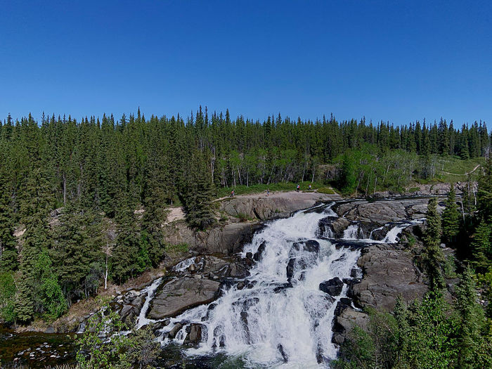 Scenic view of waterfall in forest against clear blue sky
