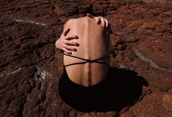 Woman embracing herself sitting on rocky land