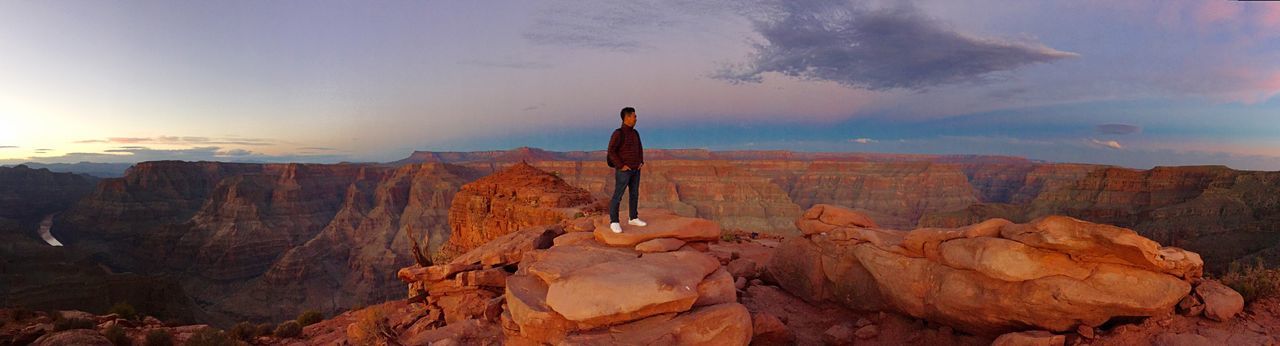 Man standing on rocks at mountain in grand canyon national park against sky during sunset