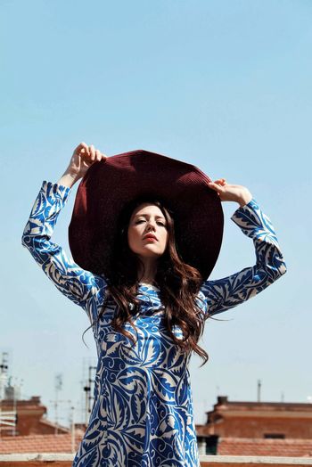 Young woman wearing hat standing against blue sky