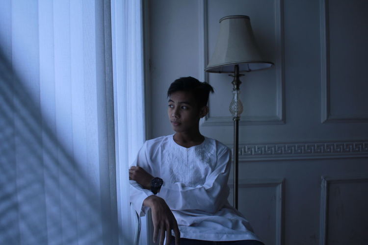 Boy looking away while sitting on bed at home