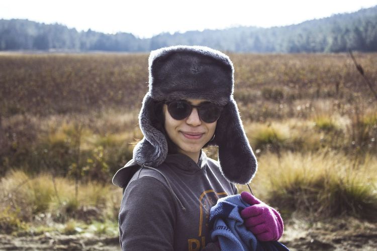 Portrait of smiling young woman holding wearing warm clothing on field