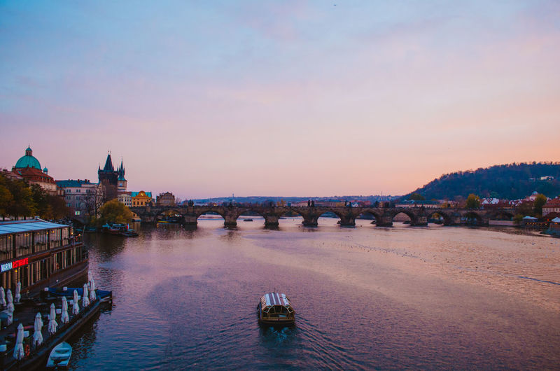 A boat crossing the vltava river during the sundown and a gradient of purple to pink colors.