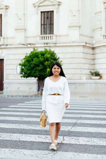 Full length portrait of woman standing against building in city