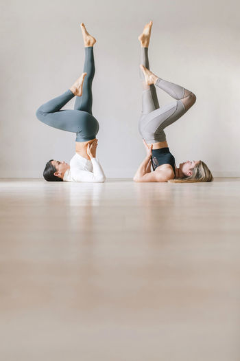 Women practicing shoulder stand in front of wall at yoga studio