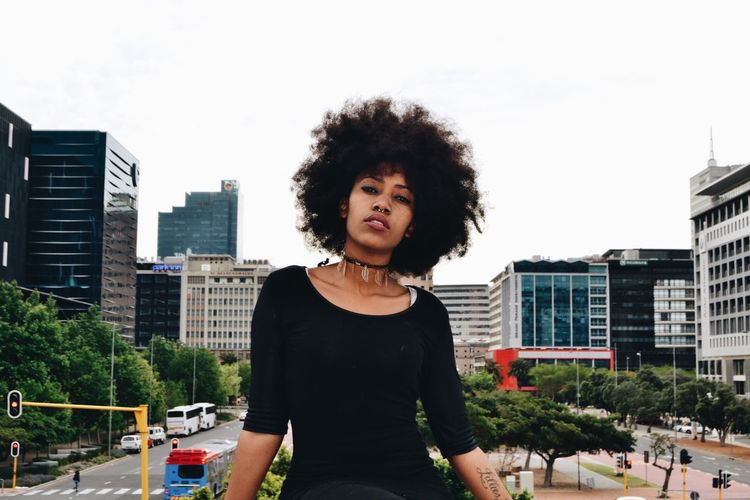 City Building Exterior Real People Portrait Young Adult Lifestyles One Person Architecture Waist Up Built Structure Looking At Camera Front View Confidence Day Standing Leisure Activity City Life Curly Hair Outdoors Sky Women Around The World The Portraitist - 2017 EyeEm Awards