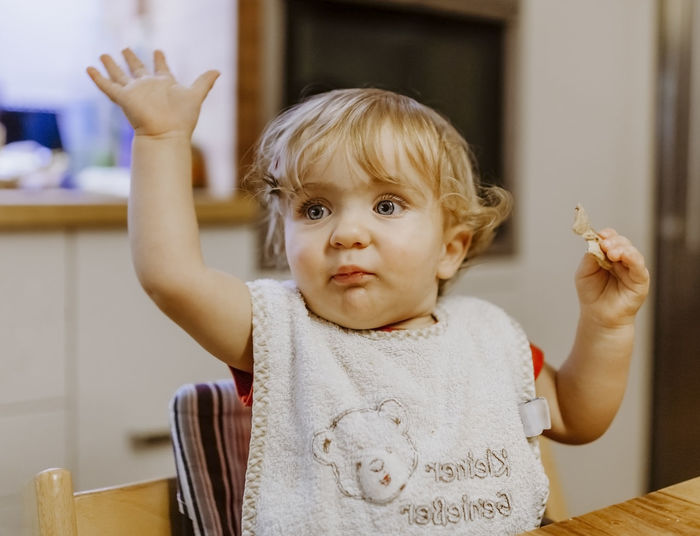 Cute baby girl looking away while sitting on chair at home