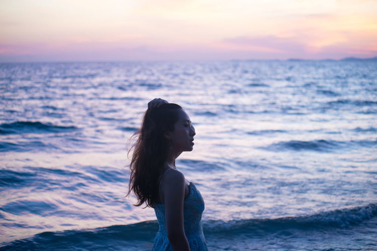 Young woman standing at beach during sunset
