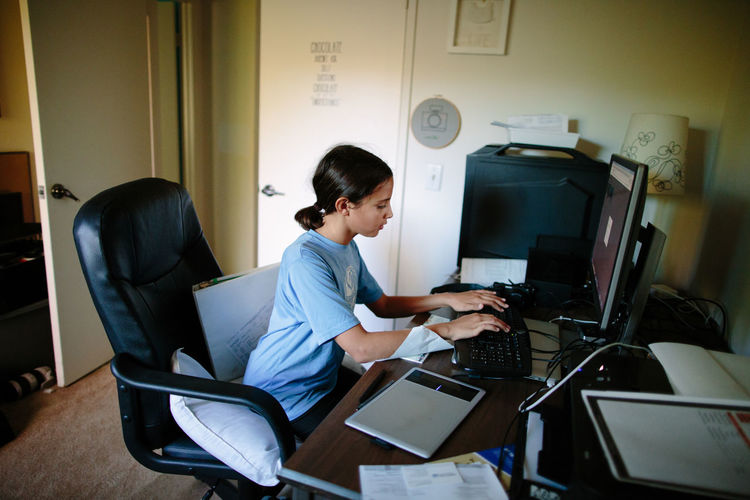 Tween girl sits at a desktop computer typing