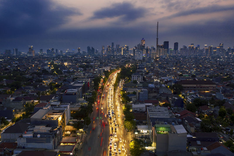 Aerial view of illuminated street amidst buildings in city at dusk