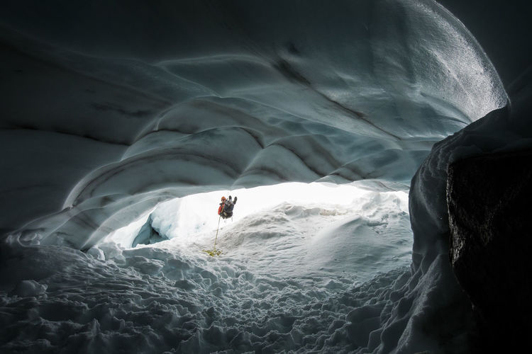 Mountaineer and explorer rappels into glacial ice cave to have a look.