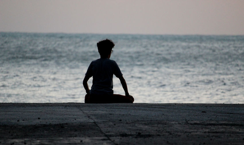 Silhouette man sitting on beach against clear sky
