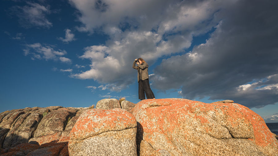 Low angle view of young woman standing on rock against sky