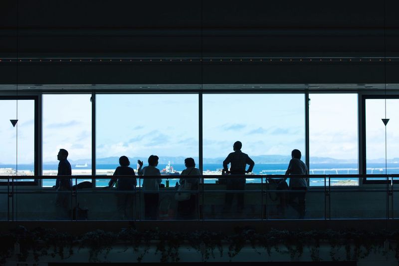 Silhouette people by railing against sky seen through glass window