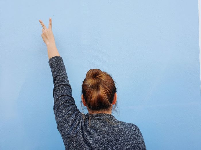 Rear view of woman making peace sign against wall