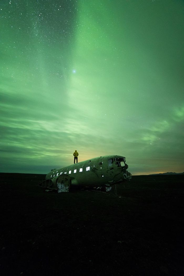Man standing on dc-3 airplane against aurora borealis at night