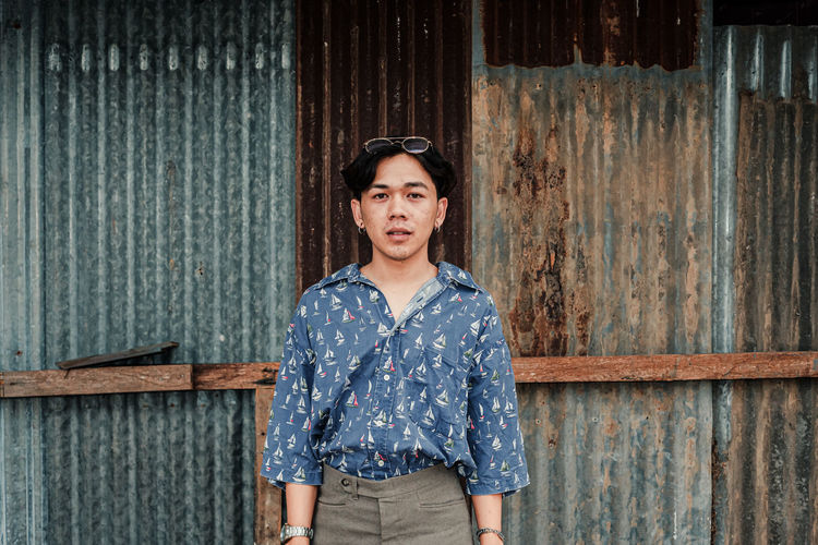 Portrait of young man standing against corrugated iron